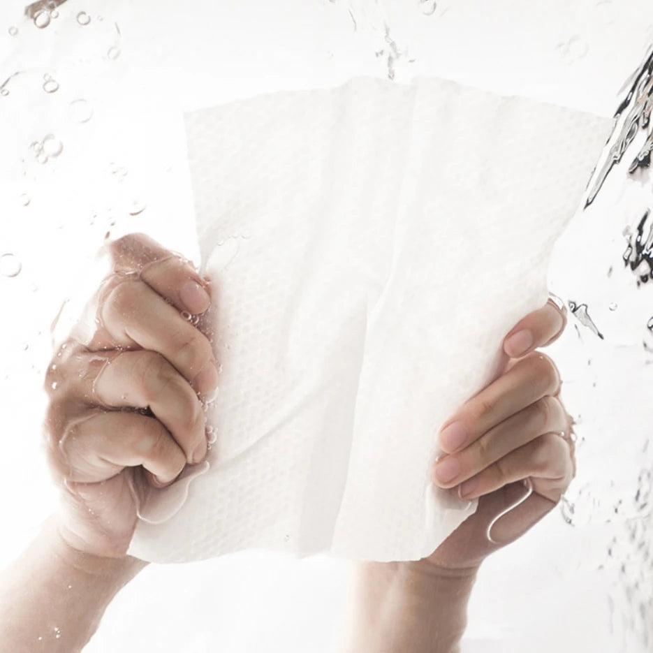 Manos sosteniendo una toalla facial desechable blanca gruesa bajo agua corriente.
