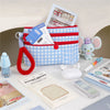 A blue and white plaid passport holder with a red strap, a sticky memo pad, and a small purple elephant toy.