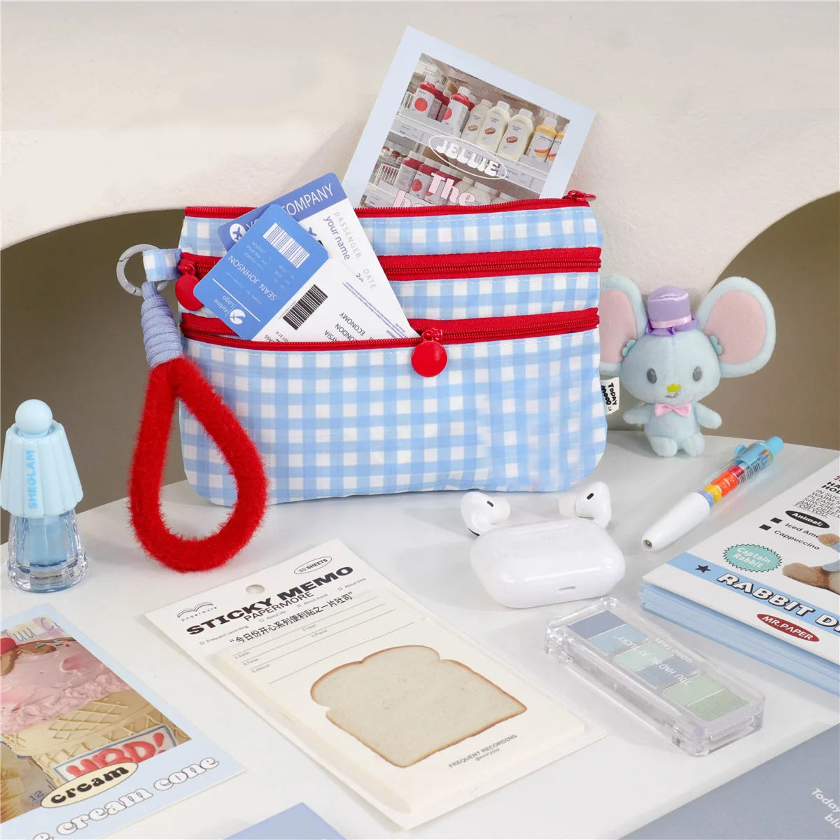 A blue and white plaid passport holder with a red strap, a sticky memo pad, and a small purple elephant toy.