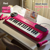 A pink electronic piano is displayed on a white table next to a microphone and music sheet.