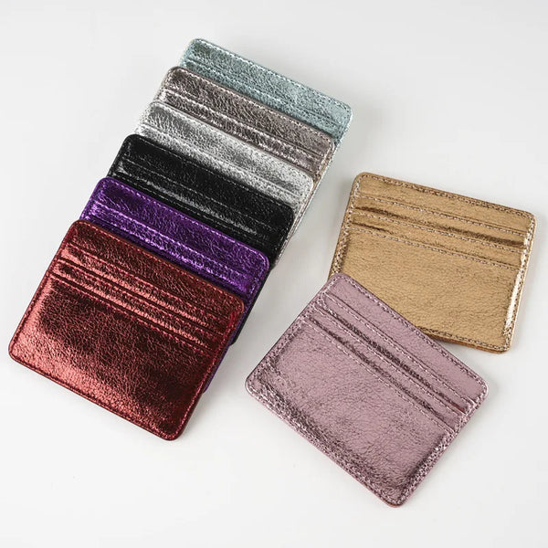 A stack of four slim leather card holders in various shades including black, purple, and gold.