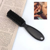 A black professional grooming brush used for styling wigs and beards, shown next to a close-up of a hand using a similar brus