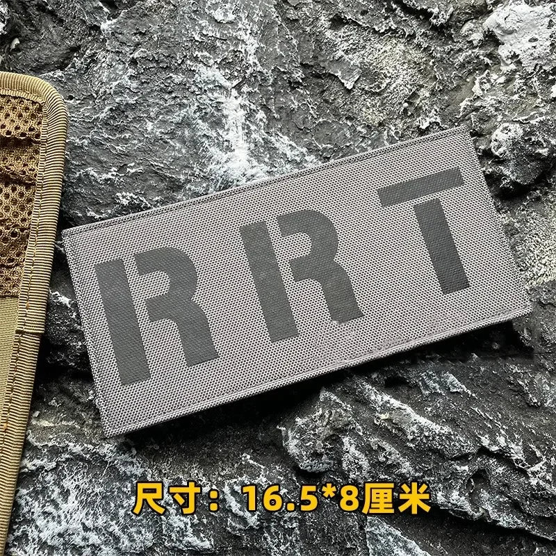 A rectangular gray tactical morale patch with the letters RRT embroidered on it, placed on a dark, rough stone surface.