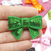 A hand holds a bright green sequin bow patch for DIY crafts.