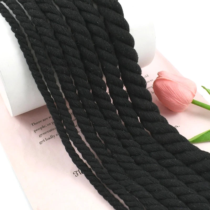A close-up of a black natural twisted cotton cord lying on a pink paper with text.
