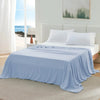 A light blue ice silk blanket is draped over a white bed with white pillows in a bright, airy bedroom setting.