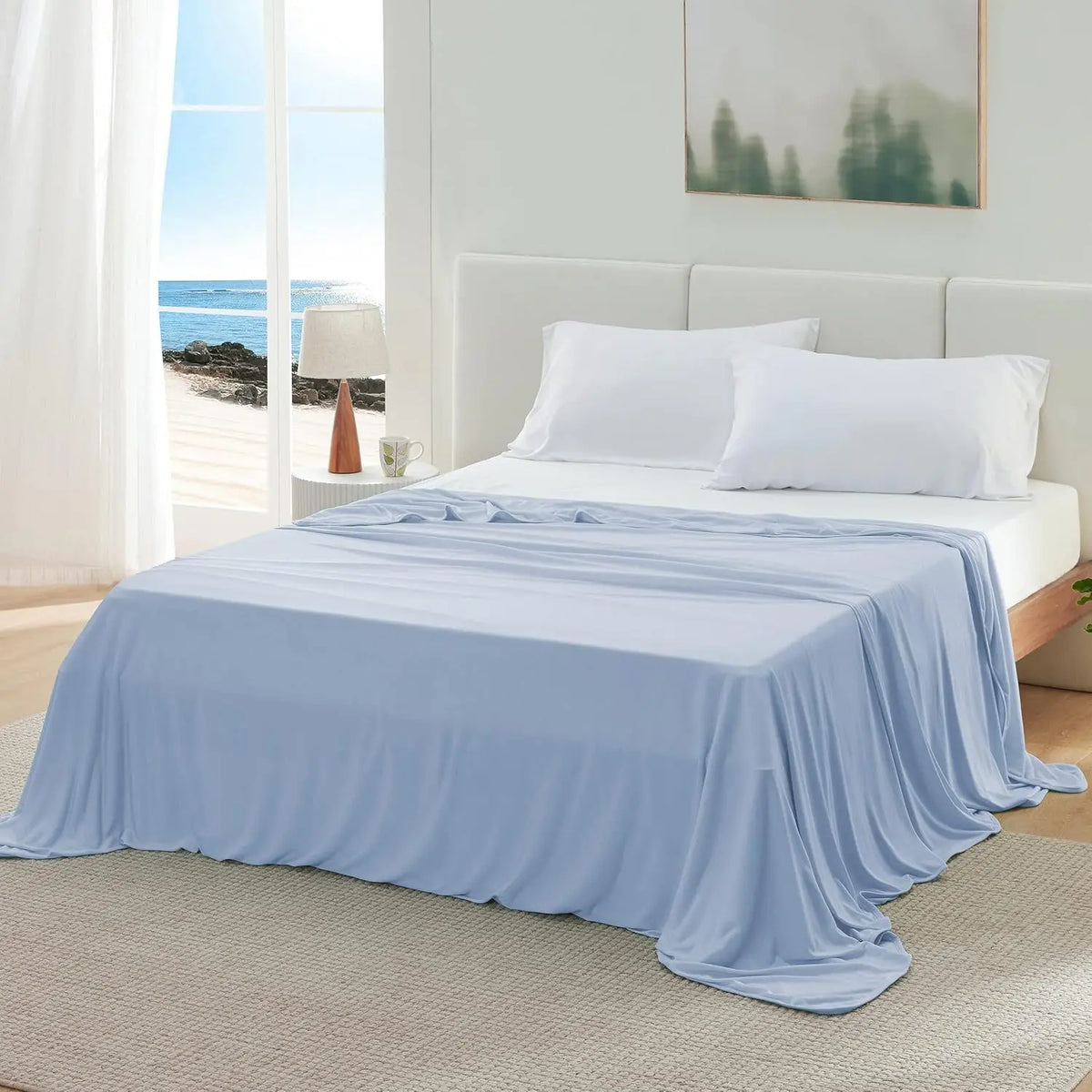 A light blue ice silk blanket is draped over a white bed with white pillows in a bright, airy bedroom setting.