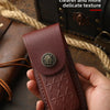 A hand holds a dark reddish-brown leather folding knife case with a decorative metal stud on top.