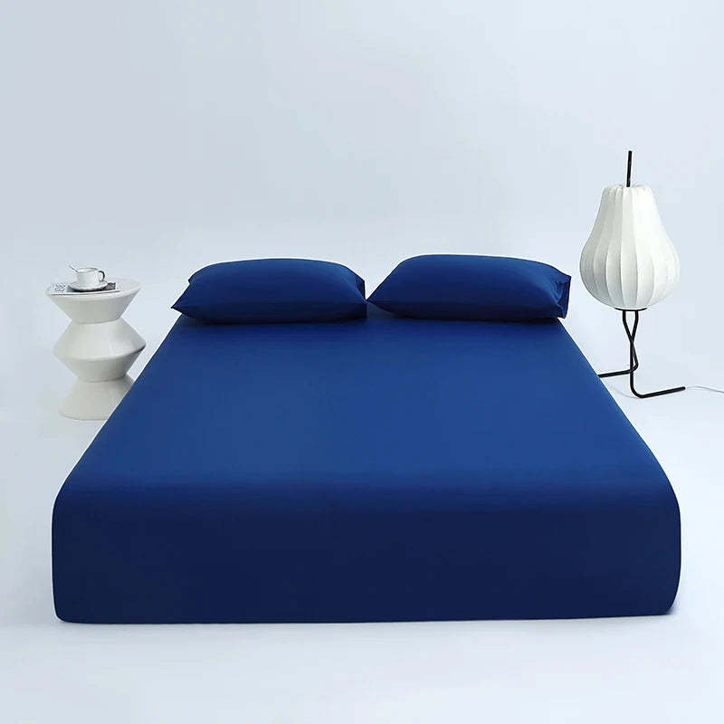 A deep blue cooling ice-silk fitted sheet is displayed on a bed with two matching pillows and a white lamp.