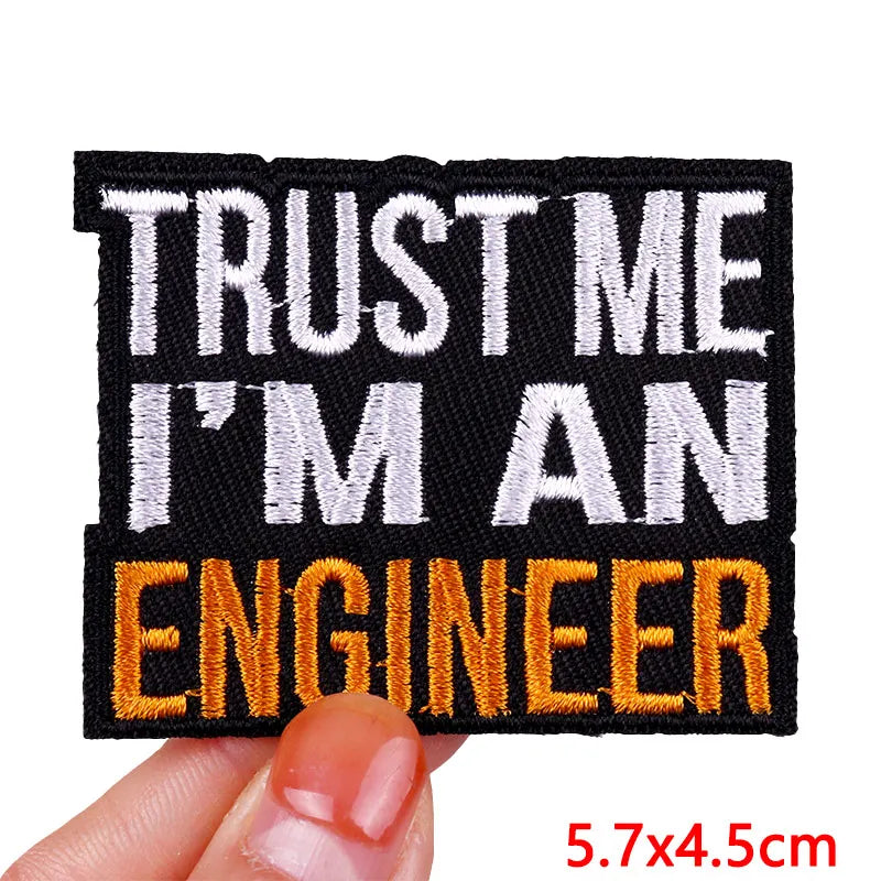 Black embroidered iron-on letter patch with white and orange text reading Trust Me I'm an Engineer