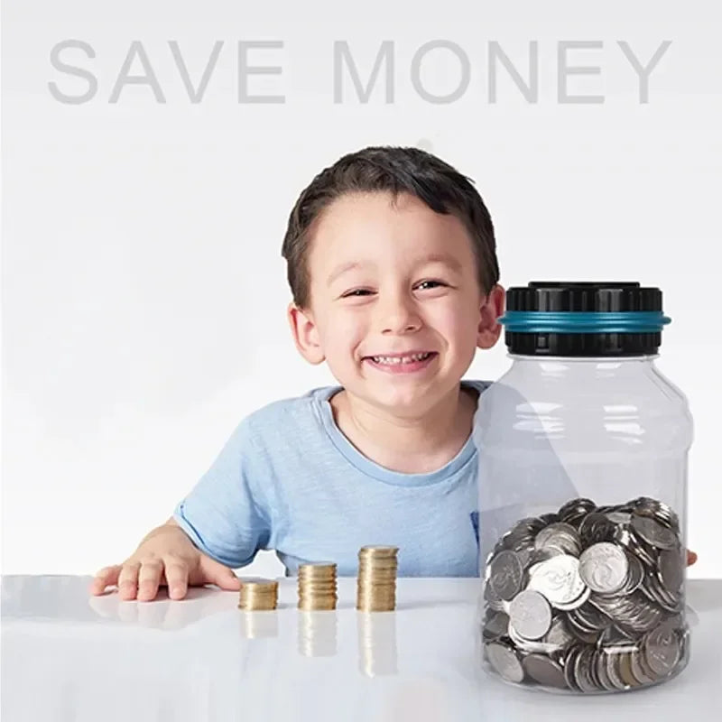A smiling boy is sitting at a table with a clear glass jar filled with silver coins and a digital coin counting piggy bank.