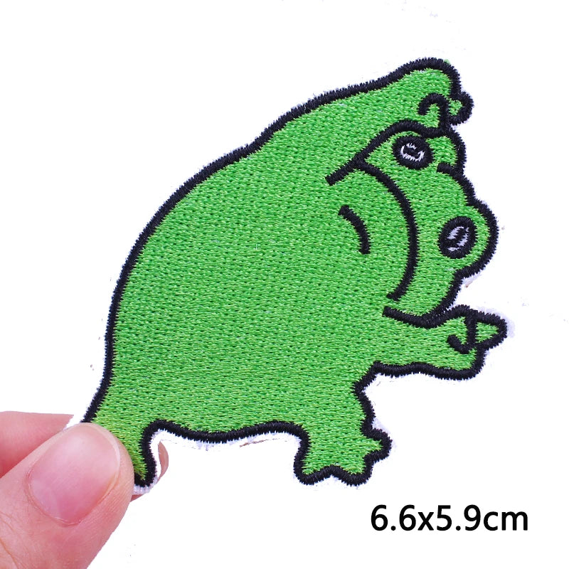 A bright green cartoon cat embroidery patch is shown being held by a finger.