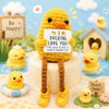 A handmade crochet pocket hug doll in yellow yarn with tiny shoes and a heart tag sitting on a white surface.