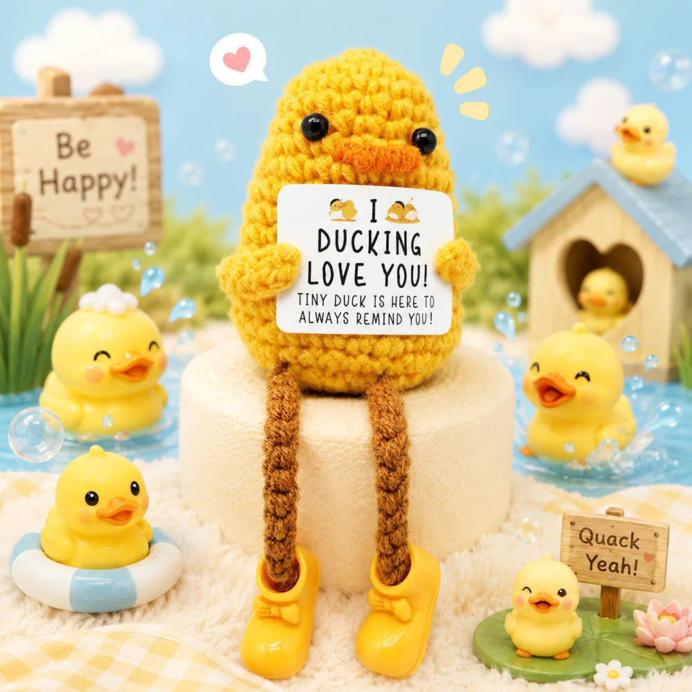 A handmade crochet pocket hug doll in yellow yarn with tiny shoes and a heart tag sitting on a white surface.