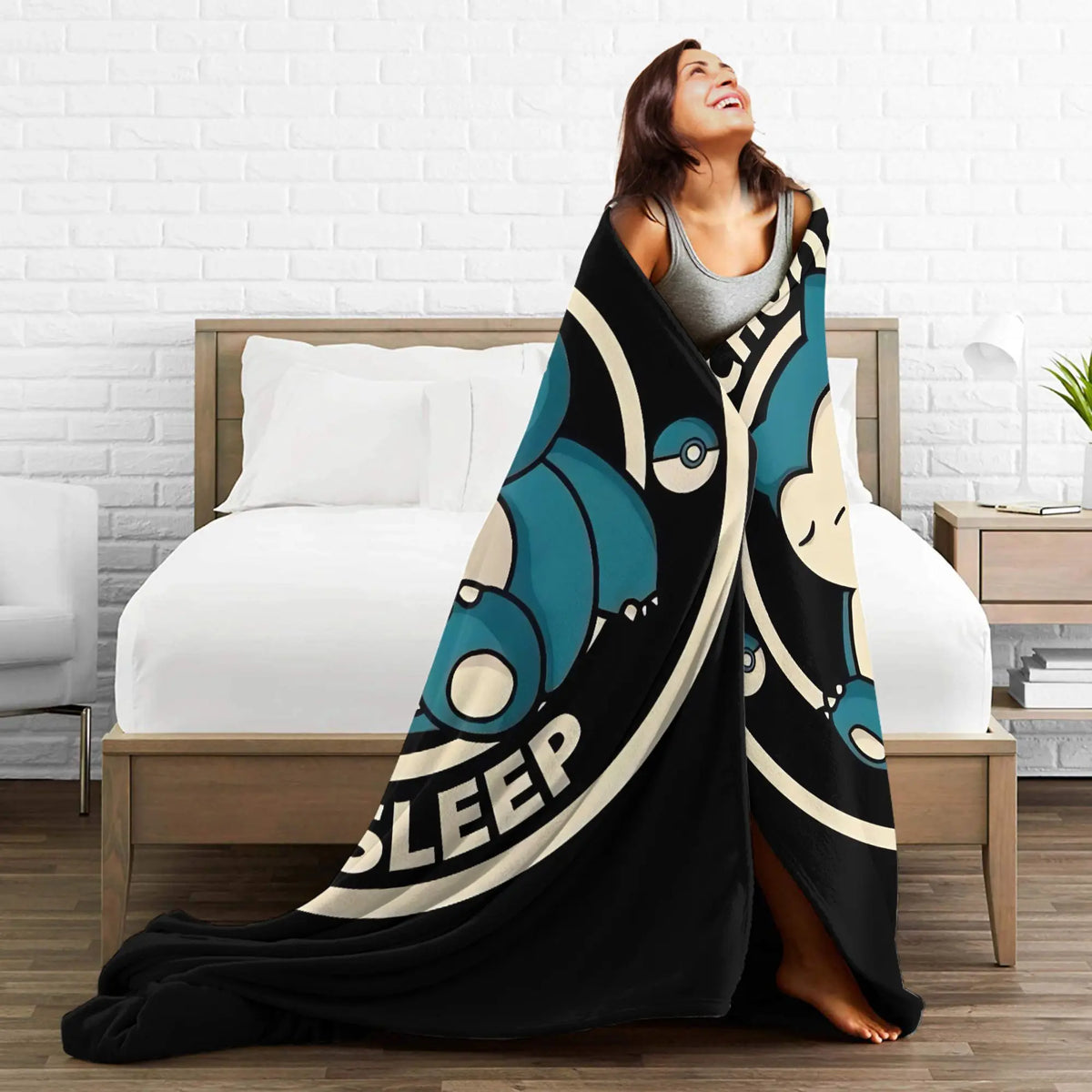 A woman is relaxing on a bed with a black and teal patterned Snorlax plush throw blanket.