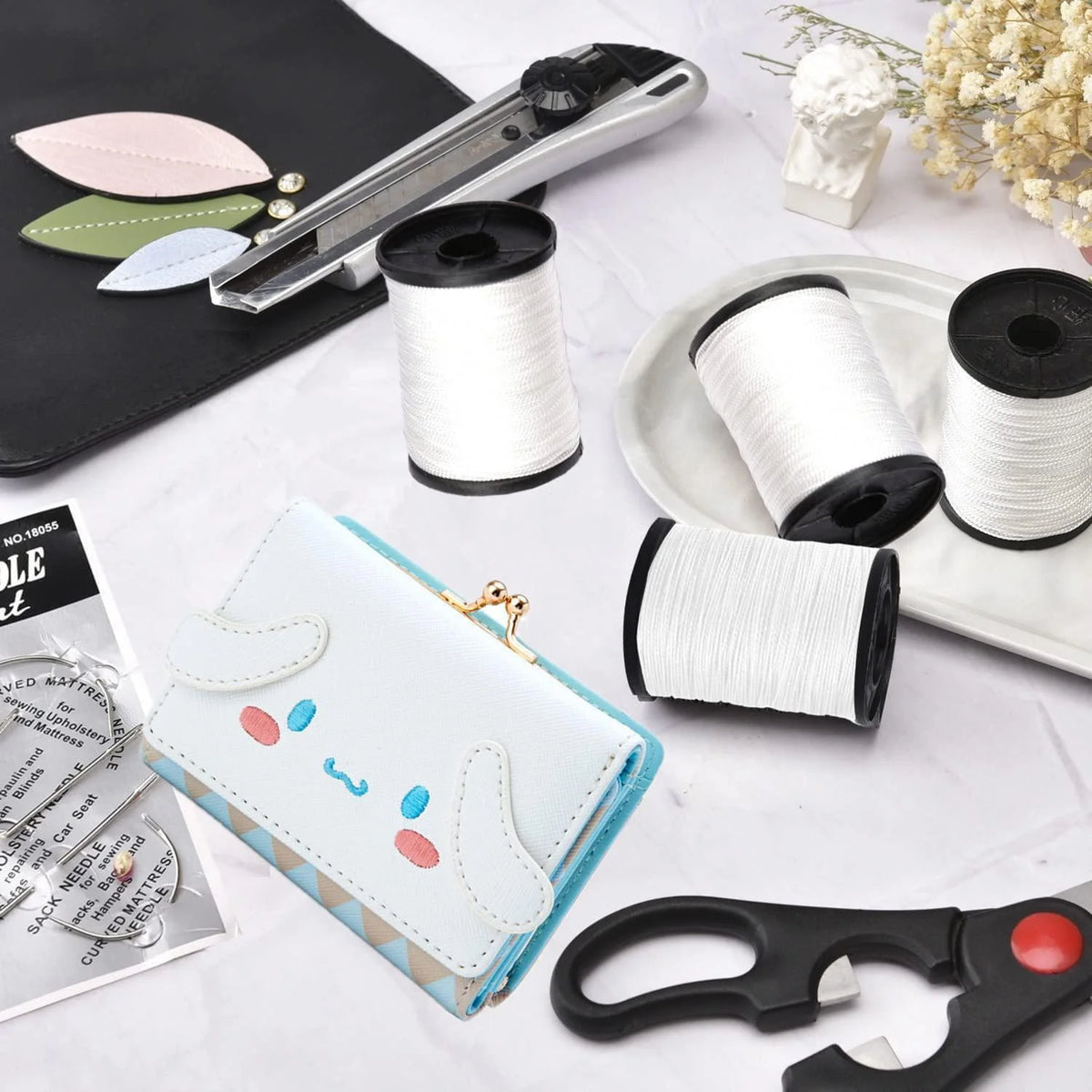 A collection of heavy duty nylon thread spools, a leather tool, and upholstery needles are displayed on a white surface.