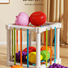 A white wooden fruit sorter cube with colorful elastic bands holding various fruits like apples and oranges.