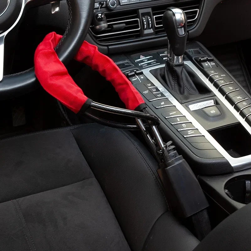 Vue intérieure d'une voiture montrant un volant avec une housse rouge et un mécanisme d'ancrage de ceinture de sécurité.