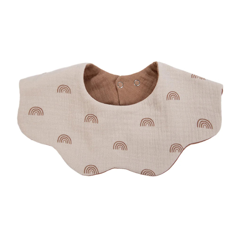 A light beige muslin cotton baby bib and burp cloth with a brown interior and small rainbow patterns.