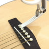 A white adjustable guitar capo with a built-in bridge pin puller is shown next to a guitar fretboard.