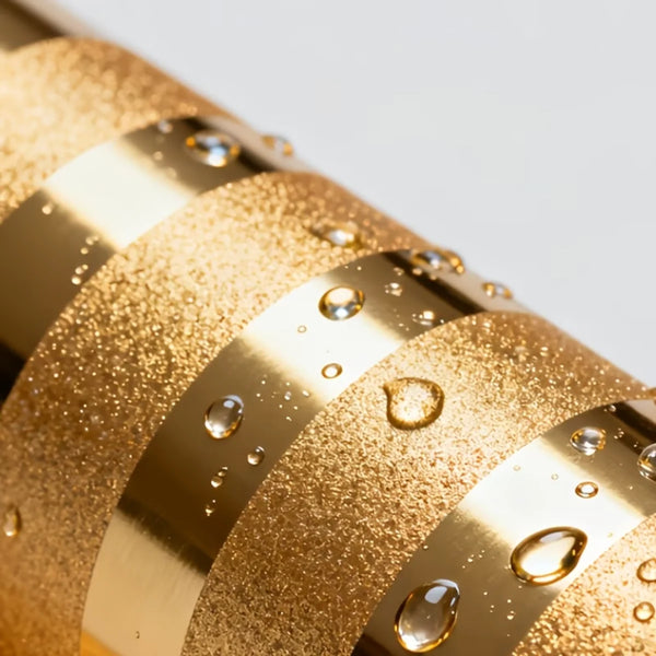 Close-up of gold textured wallpaper rolls with water droplets on a white background.