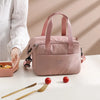 A pink compact thermal lunch tote bag with a canvas strap is shown on a white surface next to a fork.