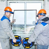Two workers in hard hats inspect a heavy-duty vacuum suction cup lifter against a window frame.