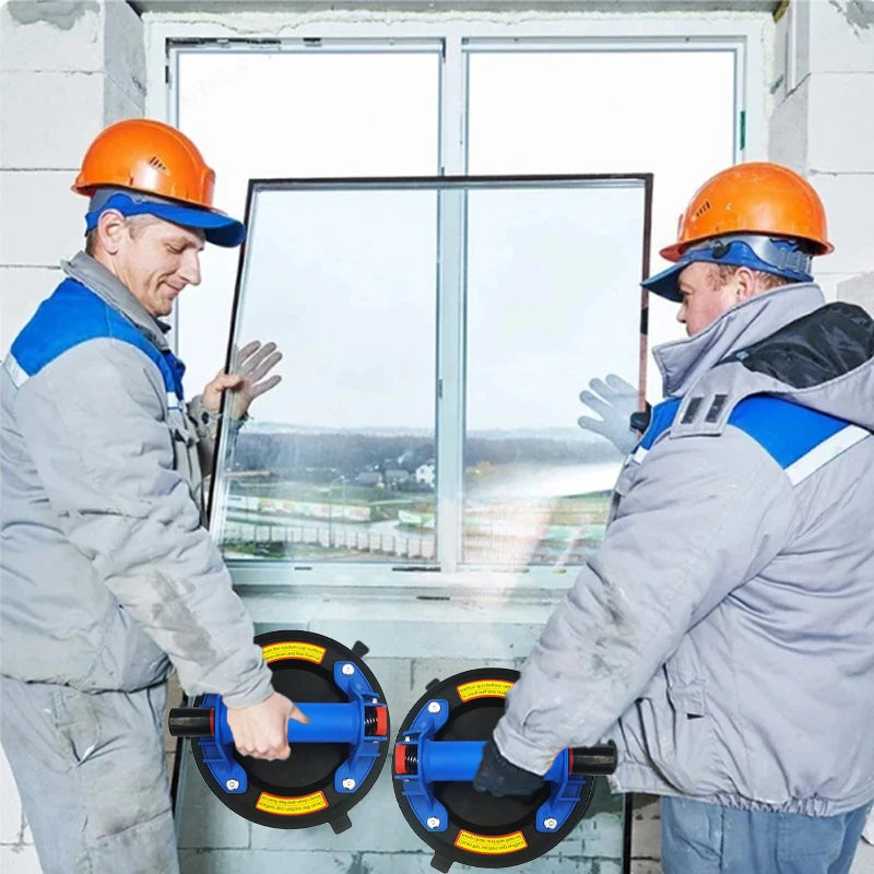 Two workers in hard hats inspect a heavy-duty vacuum suction cup lifter against a window frame.