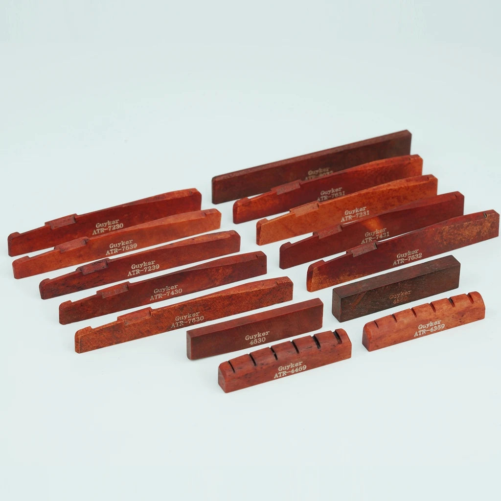 A collection of wooden cow bone acoustic guitar bridge saddles in various shades of reddish-brown.