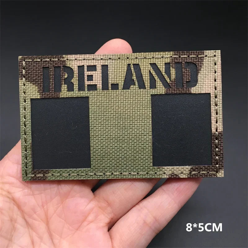 A rectangular tactical patch featuring the word IRELAND in distressed lettering on a camouflage background with two black squ