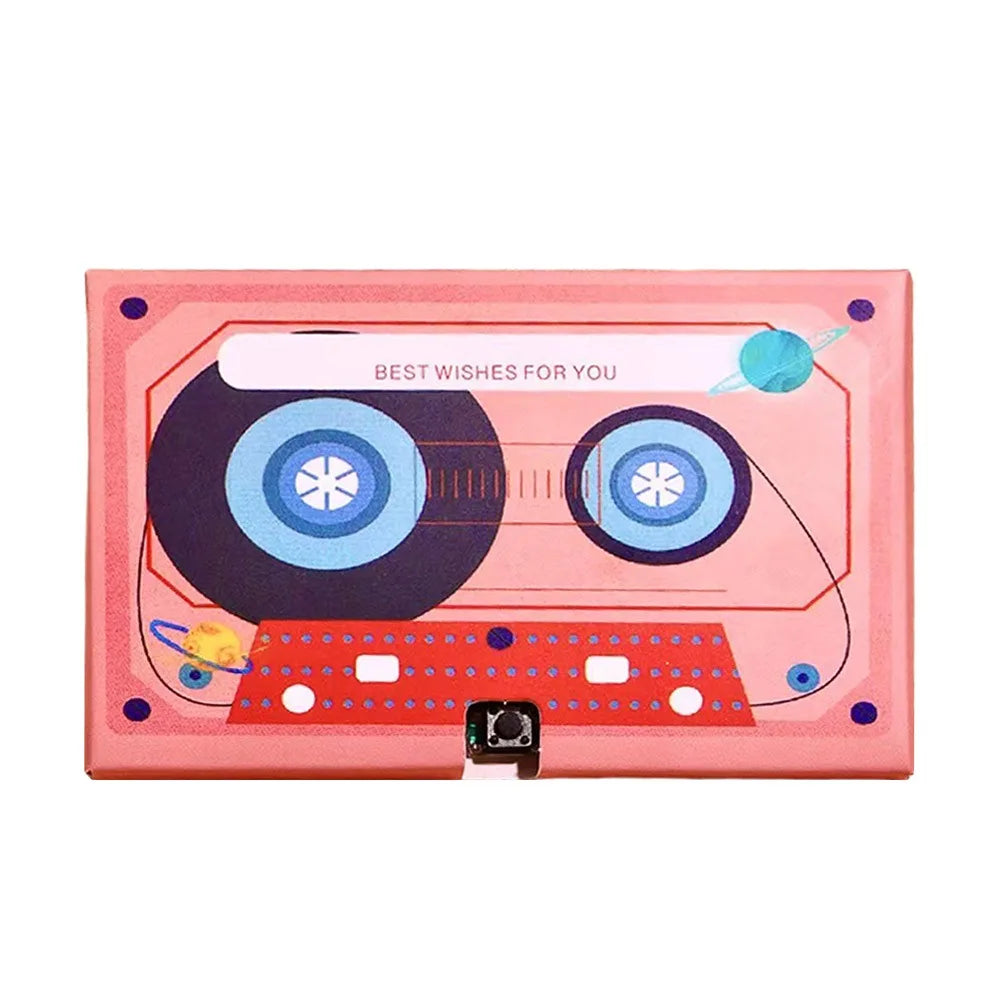 A pink greeting card with a cassette tape design featuring two circular elements and small colored accents.