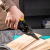 A hand is using heavy-duty aviation snips to cut a piece of wood on a workbench.
