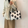 A woman holds a white blazer and beige skirt while carrying a black and white faux fur leopard print tote bag.