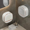 A white wall-mounted soap holder with a lid and drainage is displayed on a marble countertop.