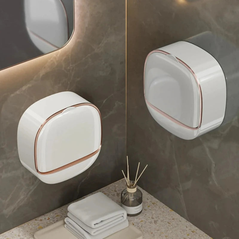 A white wall-mounted soap holder with a lid and drainage is displayed on a marble countertop.