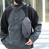 A man wearing a black waterproof jacket with a gray waist pack and a black balaclava.