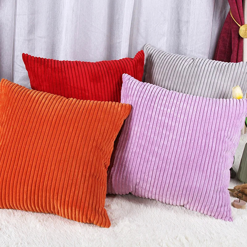 A set of striped velvet corduroy cushion covers in red, orange, and purple resting on a white surface.
