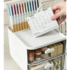 A white desk organizer with transparent drawers holds pens and a paper list.