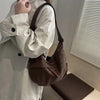 A brown leather crossbody bag is shown being held by a person wearing a light-colored jacket.