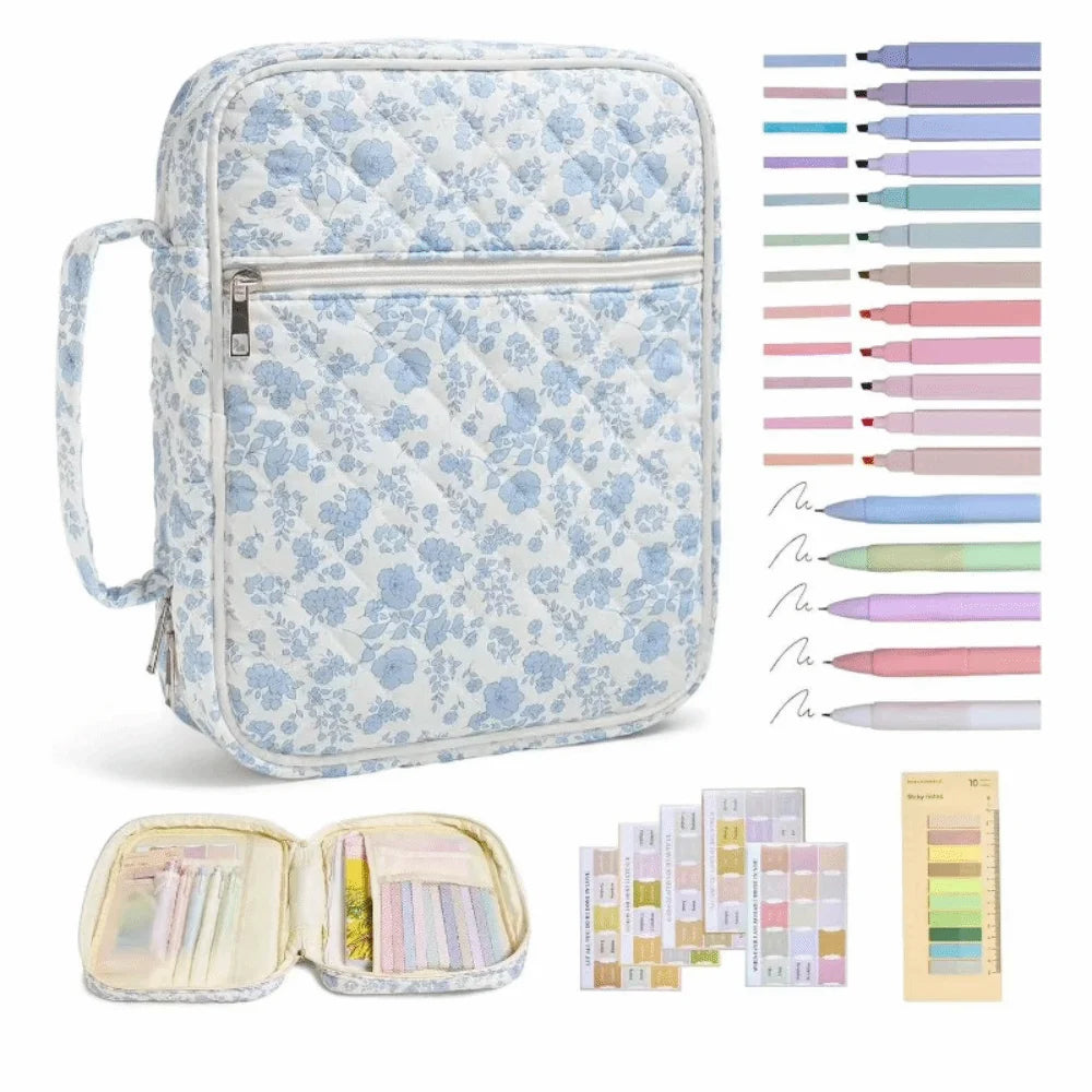 A light blue floral quilted Bible cover with a zipper pocket and carry handle, shown alongside various colored pens and a col