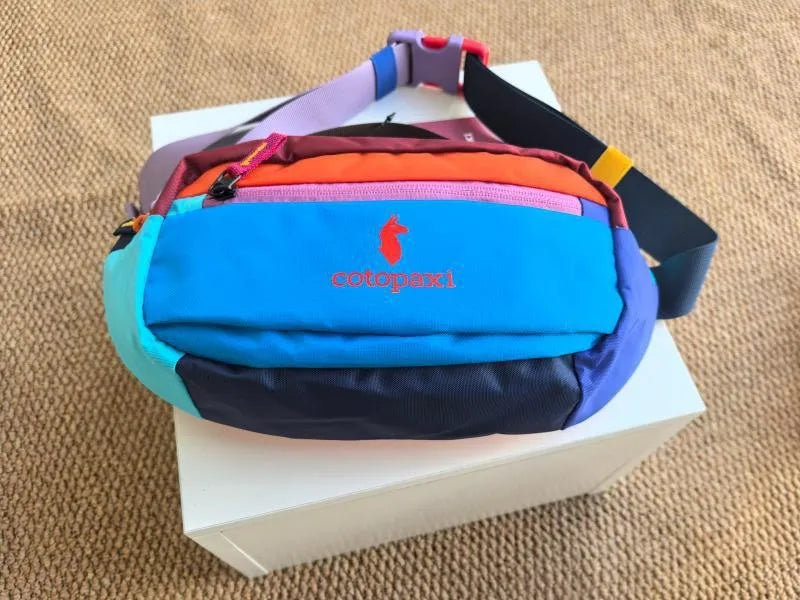 A color block waterproof nylon fanny pack featuring blue, purple, orange, and black panels resting on a white box.