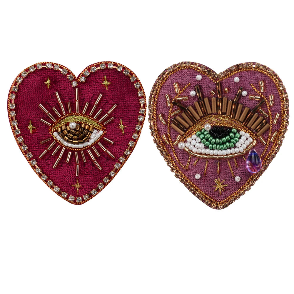 Two heart-shaped patches decorated with sparkling beads and rhinestones, featuring sunburst and eye motifs.