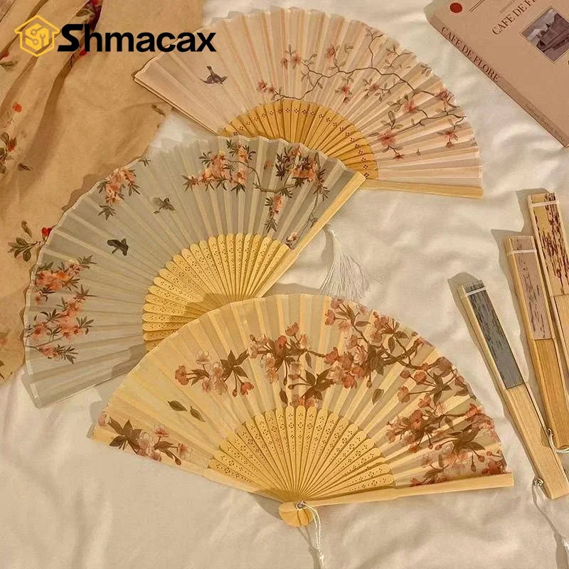 A collection of light wood folding fans with floral designs displayed on a white fabric.