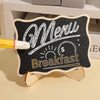 A mini wooden chalkboard sign with handwritten white text for a breakfast menu is displayed on a light surface.