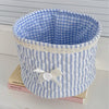 Cesta de costura con forma de corazón a rayas azules y blancas sobre una superficie blanca.