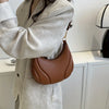 A close-up of a brown leather textured crossbody bag with a gold chain strap worn by a person in a light beige blazer.