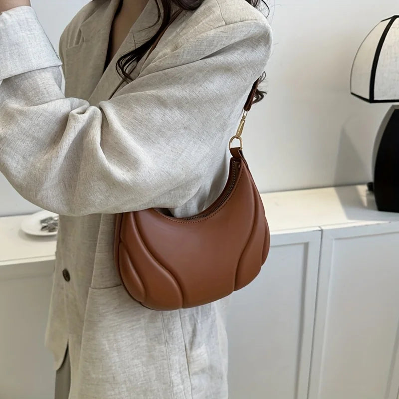 A close-up of a brown leather textured crossbody bag with a gold chain strap worn by a person in a light beige blazer.