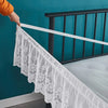 White ruffled lace bed skirt hanging over a dark metal bed railing against a teal wall.