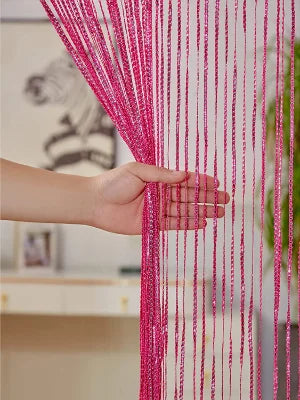 A hand is pulling a vibrant pink tassel string curtain, made of fine threads, across a doorway.