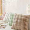 A collection of fluffy decorative pillow covers in pastel shades lined up on a white surface.